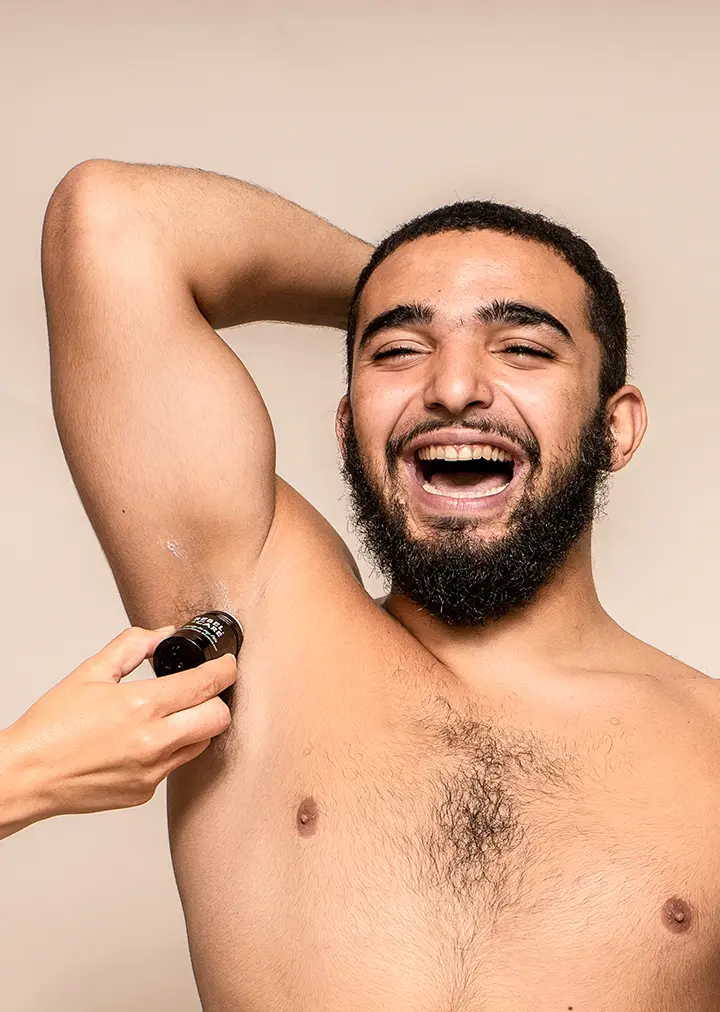 Topless man applying deodorant while laughing